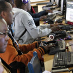African adult is reading a digital book from an international library on a computer.