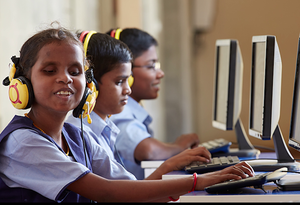 Three children sit at computers listening to Bookshare accessible ebooks through headphones.