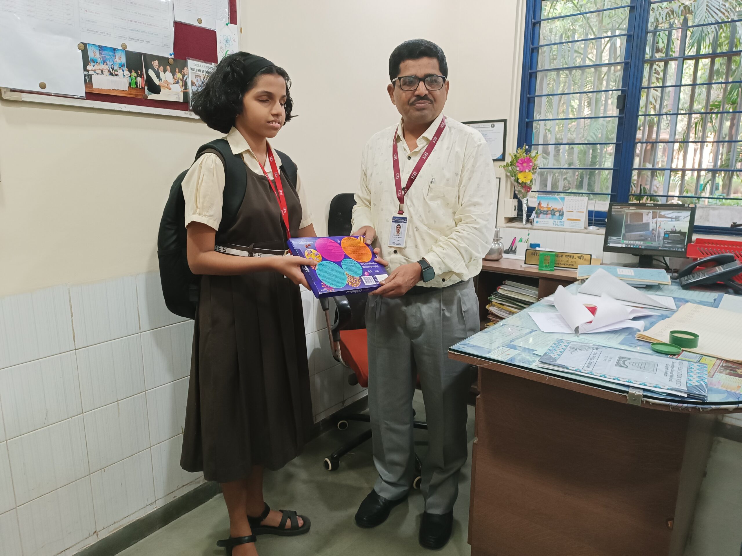 Rujul and Principal of IES Mulund pose for a photo in classroom near desk..