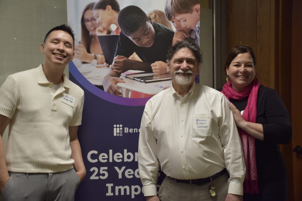 Benetech staff smile in front of a “25 Years of Impact” banner.