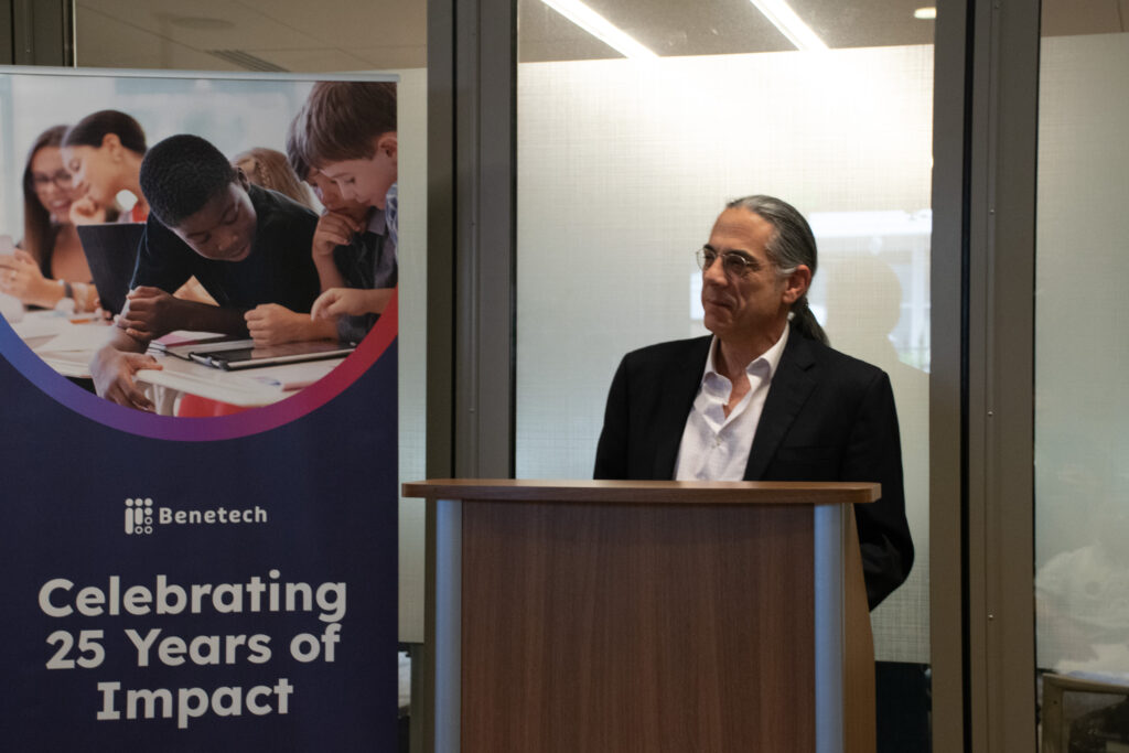 Richard Mueller, Chairman of the Board, speaks at a podium next to a Benetech banner celebrating 25 years of impact.